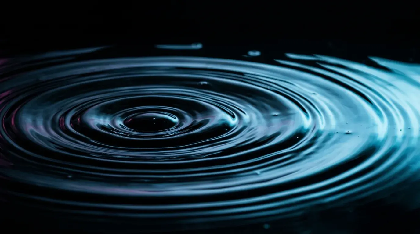 Concentric ripples spreading outward across the surface of dark water, lit from the right in pale blue