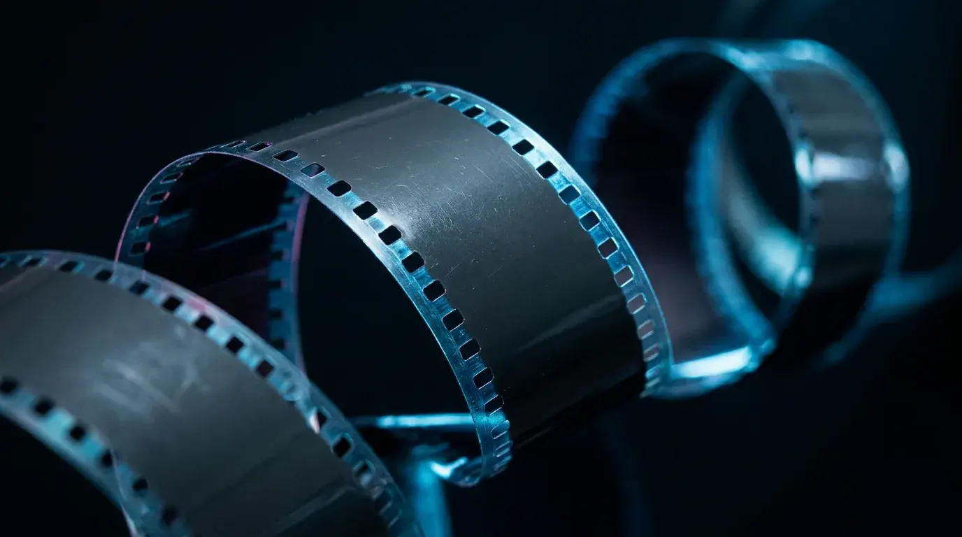 Loops of 35mm film curling through darkness, the sprocket holes along both edges catching blue light
